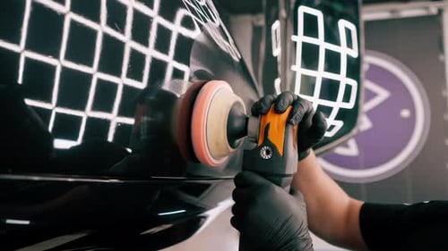 Close-up of a car wash worker using a polishing machine to polish the hood of black luxury car