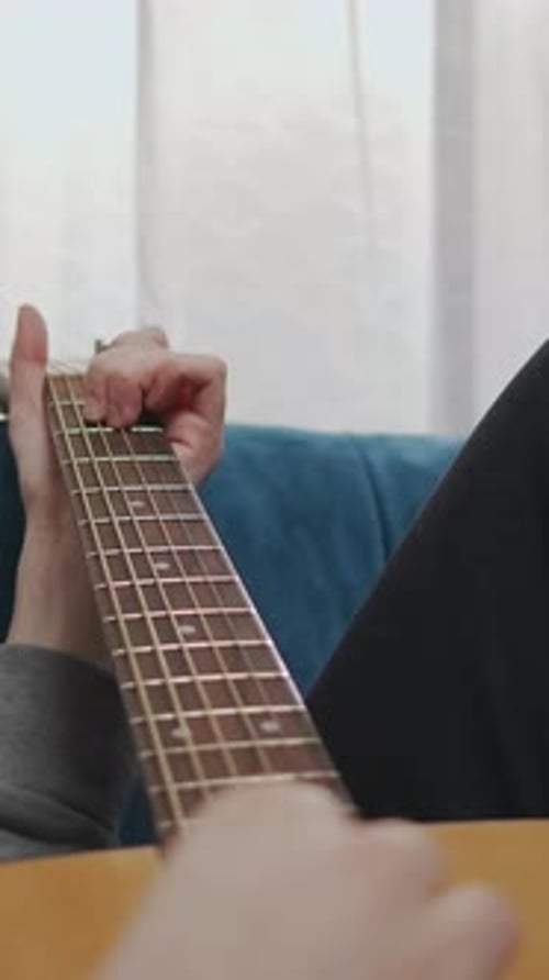 Relaxed Closeup Perspective of a Person Lying on a Couch and Practicing Gentle Guitar Chords