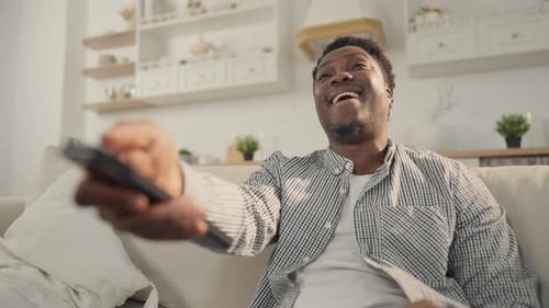 Man Laughing While Relaxing on Couch with Remote