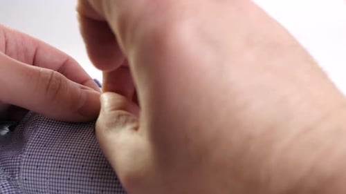 K63. The man manually sews a button on the sleeve of his shirt. Self-service. Small household chores