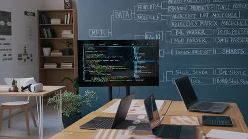 Screen with Computer Code and Laptops on Desks in Programming Class