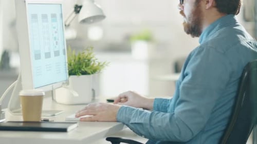 In the Creative Agency Office. Bearded Man in Glasses Works at the Desktop Computer. Camera Moves F