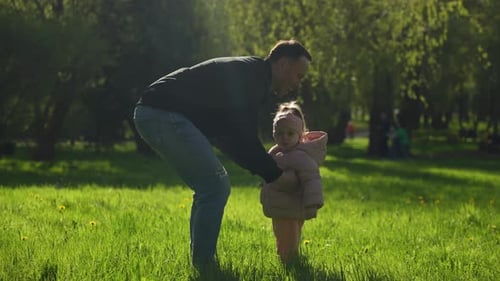 Father Lifts Little Daughter High in Sunlit Park Joyful Moments