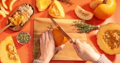Woman cutting pumpkin on orange background, above view