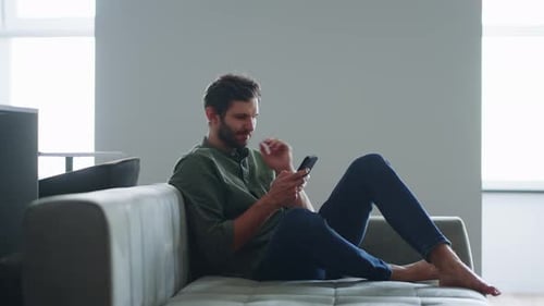 Man Relaxing with Smartphone on Couch at Home