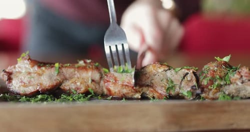 Cutting Grilled Meat on Wooden Board with a Fork