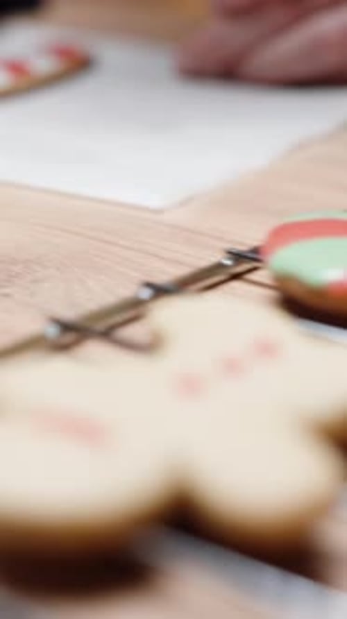 Vertical video. Using white icing from a small bag, the woman covers the gingerbread cookie in the s