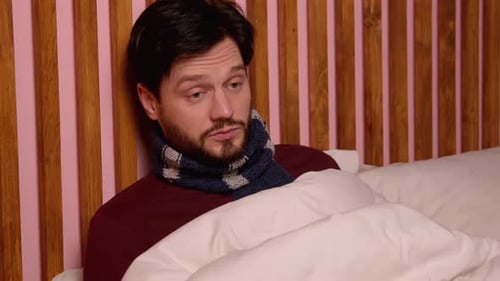 Man Sick in Bed Blowing Nose With Tissue