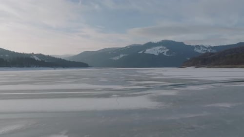 Frozen lake surrounded by snowy mountains under a soft winter sky, peaceful scenery