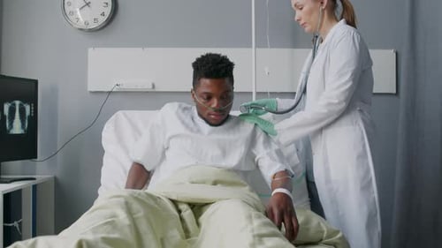 Doctor Examines Patient Lying in Hospital Bed