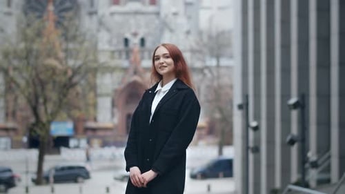 Smiling Young Woman in Black Coat Standing on Blurred City Background Urban View with Ginger Lady