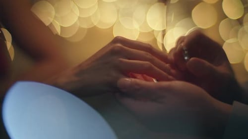 Mann trägt Ehering am Finger einer Frau in Nahaufnahme von verschwommenem Licht am Abend
