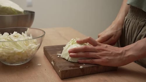 Nahaufnahme eines Kochs, der mit einem Messer sorgfältig frischen Weißkohl auf einem Holzbrett hackt