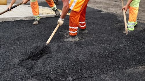 The Road Construction Team Uses Shovels to Distribute New Asphalt at the Construction Site