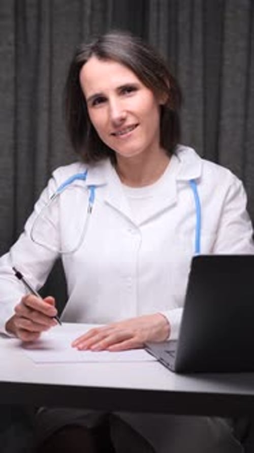 Vidéo verticale Femme médecin travaillant à son bureau écrivant sur des documents avec un ordinateur portable et des dossiers