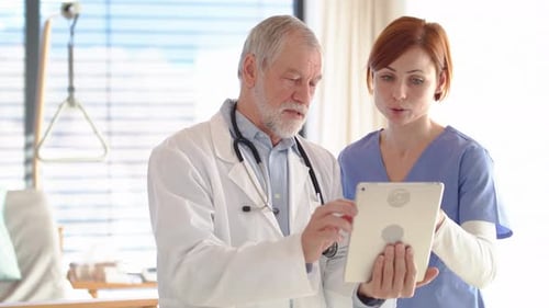 Senior doctor discussing patient care with nurse using tablet in hospital
