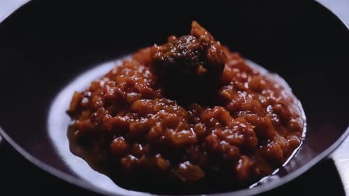 Meatballs being placed in brown sauce on plate