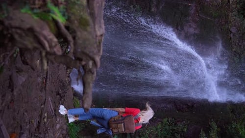Back view of young woman standing in front of waterfall.