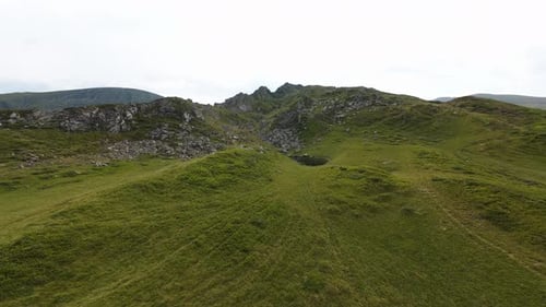 Mountain landscape with green and rocky hills highlighting a small lagoon where the sky is reflected