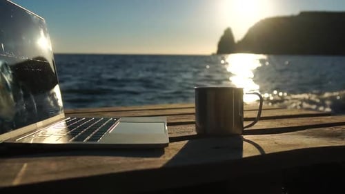 Silhouette of Laptop and Cup on the Beach Over Sea Sunset