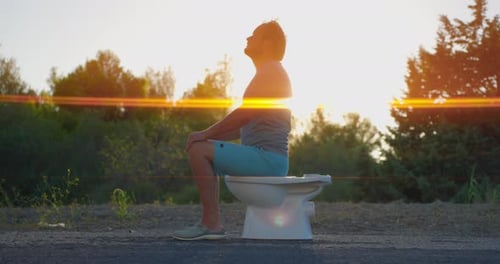 O homem sentado no banheiro no fundo do pôr do sol