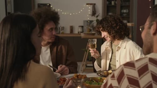 Four Friends Sharing Candlelit Meal, Raising Glasses in Toast and Laughing