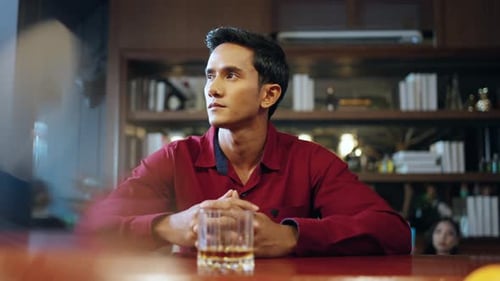 4K Loneliness Asian man drinking whiskey at bar counter alone.