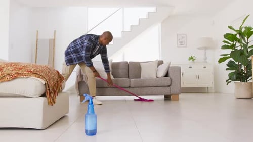 African American man holding pink mop cleaning tiled floor at home for deep cleaning