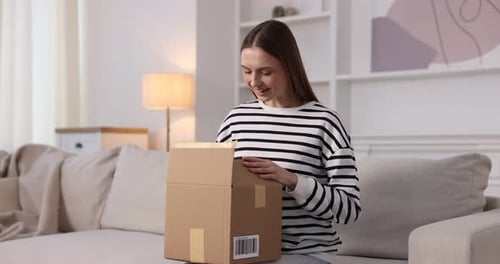 Woman opening parcel on sofa at home