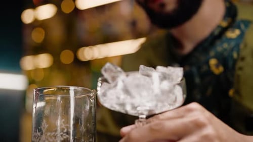 close-up of a bartender pours ice cubes into a cocktail glass in preparation of delicious cocktails