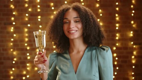 Jolie femme aux cheveux noirs bouclés en robe argentée en soie avec une coupe de champagne