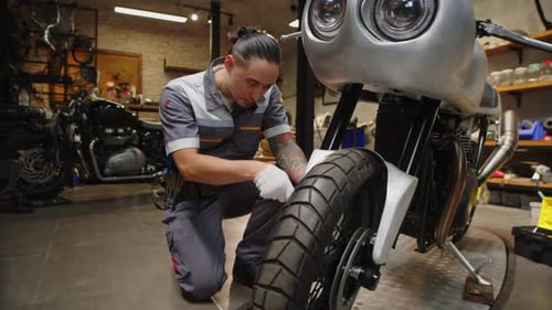 Repairman Examining Wheel of Motorcycle and Smiling at Camera