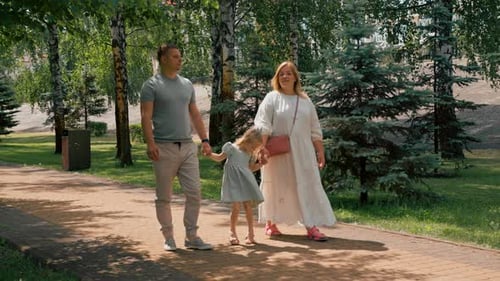 Little cute girl in green summer dress with parents in city park on a walk summer family lifestyle