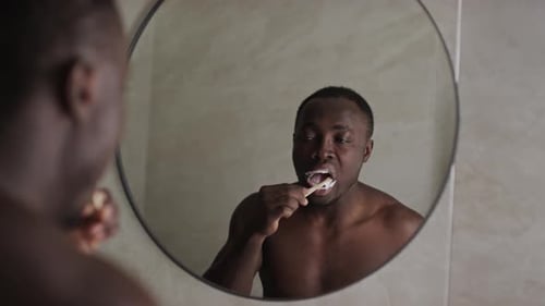 African American Guy Brushing Teeth in Front of Mirror in Morning