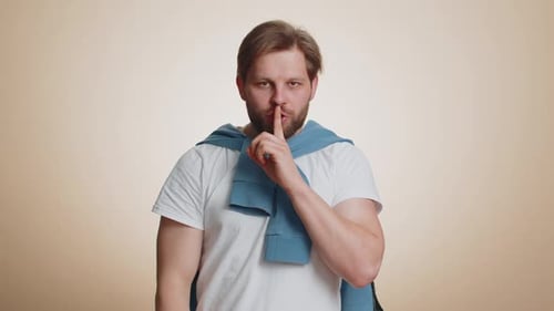 Junger bärtiger Mann drückt den Finger auf die Lippen und macht Schweigen, Geste, nicht verraten, Geheim, Klatsch und Tratsch