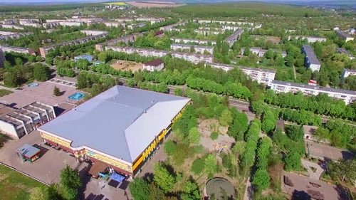 Large roof of a rectangular building in the city. Residential areas with lots of green trees.