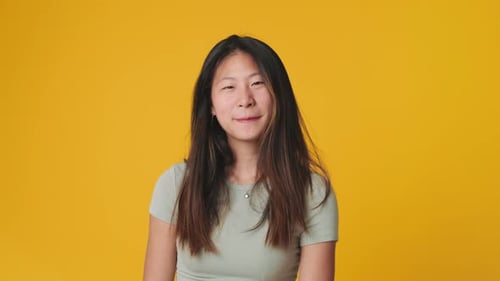 Young woman looking at camera, smiling and flirting isolated on yellow background in studio