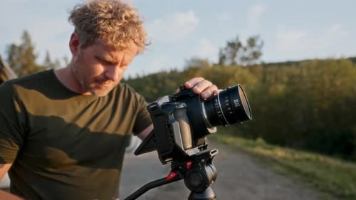 Man Adjusting Camera on Tripod in Rural Setting
