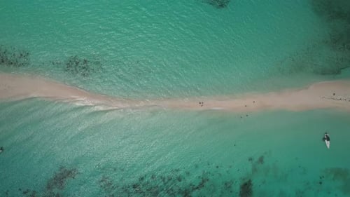 A thin sandbar in turquoise waters with people walking and a kayak nearby, aerial view, timelapse