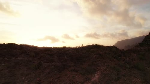 Woman running along the edge of cliff at sunset with the sky painted in warm hues. Tenerife Canary I