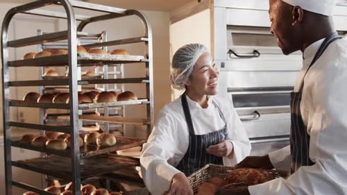 Happy diverse bakers working in bakery kitchen, holding fresh bread and talking in slow motion