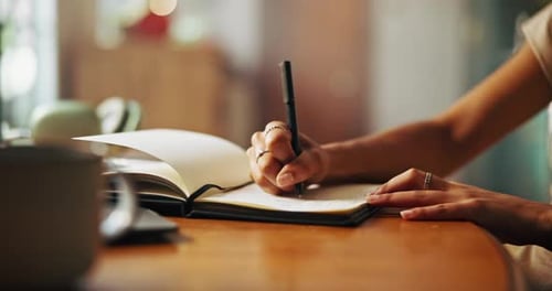 Person Writes in Journal on Wooden Table Indoors