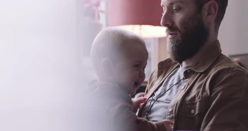 Single father comforts crying baby boy sitting on lap