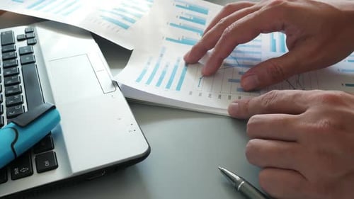 Analyzing Data Charts on Desk Next to Laptop