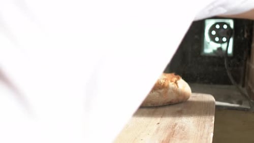 Nahaufnahme, Bäckerhand mit Handschuhen nimmt Laibbrot aus der Schale und legt es daneben