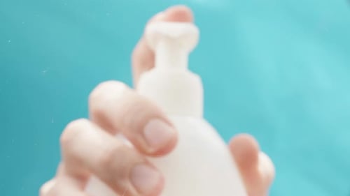 Low-angle view focused on the window. Squeezing liquid soap from a bottle on a blue background.