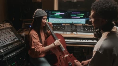 Woman plays cello while musician watches in studio