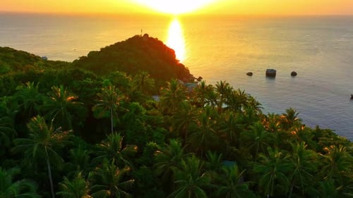 Aerial drone is flying along the coast of a tropical island at sunset.