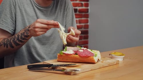 Man Adding Cheese to a Sandwich