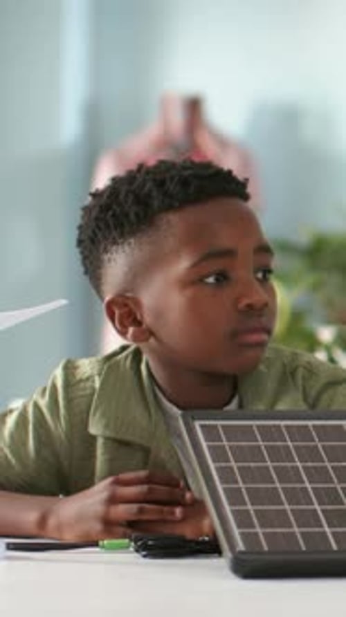 Vertical video: Responding to off-camera cue, student turning head at study table, with solar panel